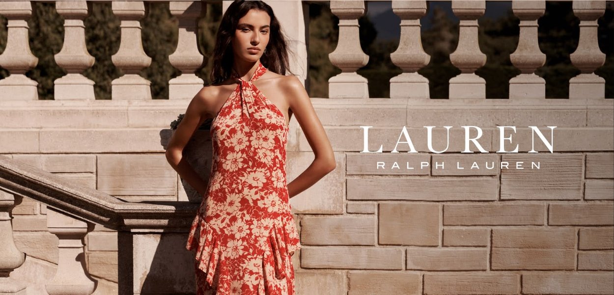 Mujer con vestido rojo de flores sin mangas, apoyada en una barandilla de piedra con el logo "Lauren Ralph Lauren" a la derecha.