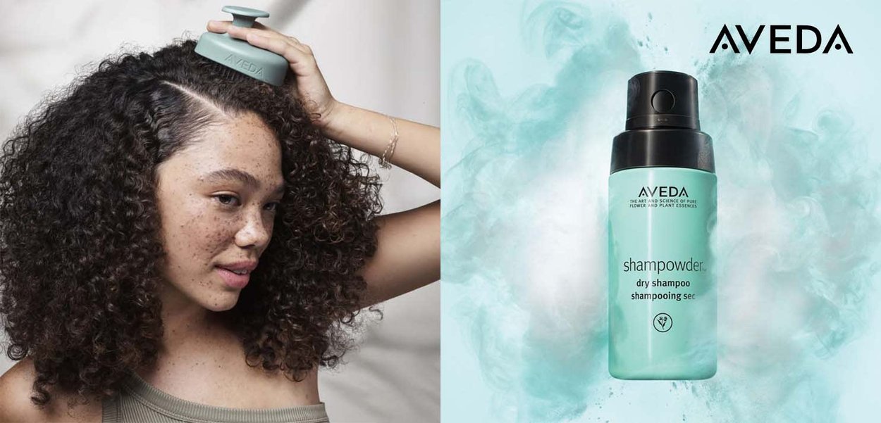 Aveda Shampowder torrshampo i en mintgrön behållare med svart pump, med ljus akvafarben dimma i bakgrunden. Modell med lockigt hår och fräknar.
