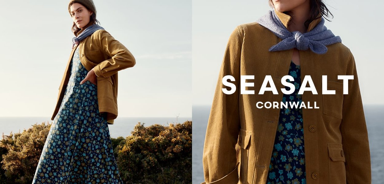 Light brown corduroy jacket, floral blue dress, soft gray scarf. Text reads "SEASALT CORNWALL." Simplified environment with ocean view.
