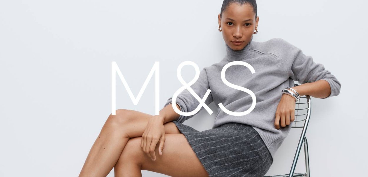 Szary sweter z dzianiny o prążkowanej fakturze, zestawiony ze spódnicą w szare paski. Modelka siedzi na krześle z drutu, na którym nałożono wyraziste logo "M&S".