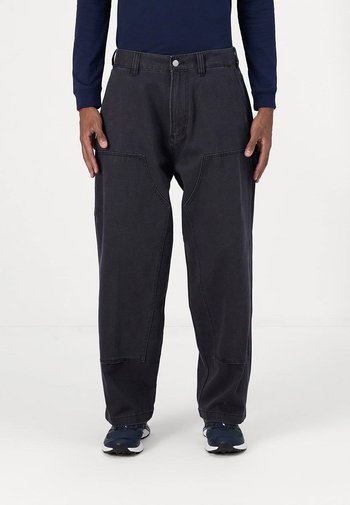 Zwarte denim broek met een losse pasvorm, voorzien van grote zijzakken en contrasterende stiksels. Gecombineerd met een marineblauw T-shirt met lange mouwen en sneakers.