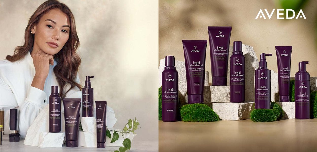 Produits de soins capillaires Aveda dans un emballage violet foncé, disposés sur des pierres claires et texturées, accompagnés de verdure et d'un modèle en tenue blanche.