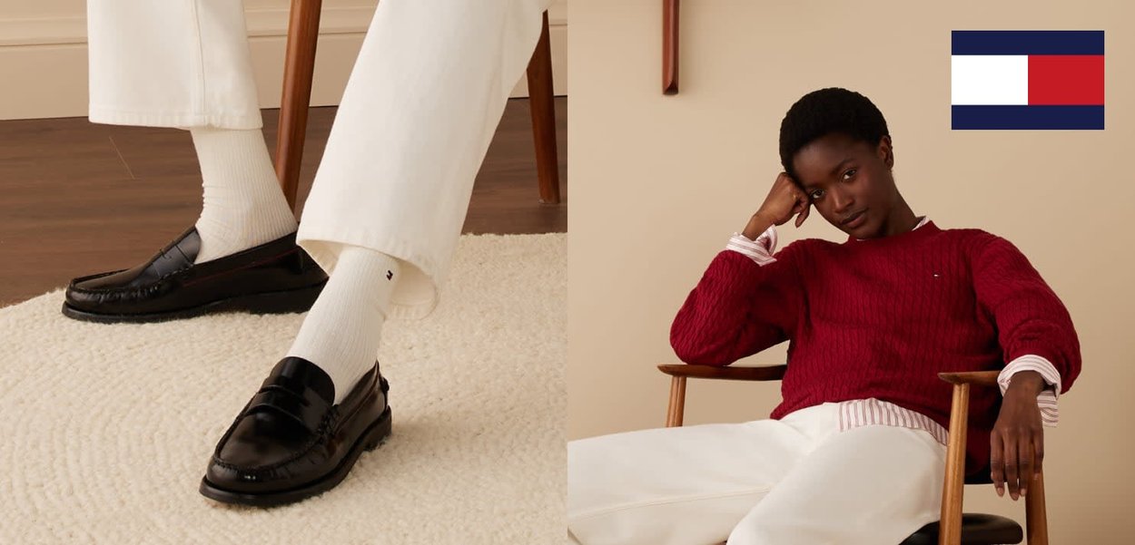 Zwarte leren loafers met een mocassindesign, gedragen met witte geribbelde sokken; een model in een rode kabelgebreide trui zittend op een houten stoel.