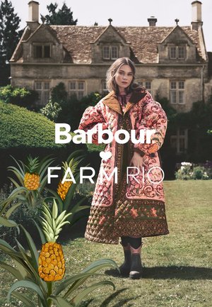 Pink quilted coat with floral and pineapple patterns, brown suede collar, paired with black rubber boots. Greenery in the background.