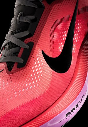 Primer plano de una zapatilla de correr Nike roja con el logo negro, cordones grises y suela blanca etiquetada "Air Zoom Full Length."