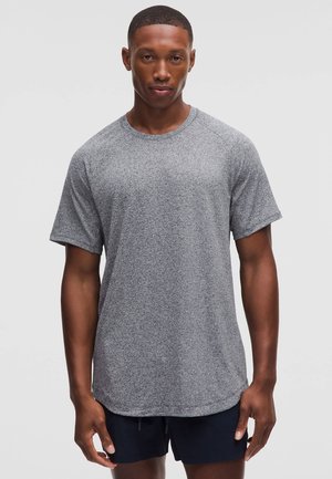 Harmaa, lyhythihainen urheilupaita, joka on valmistettu tekstuurillisesta kankaasta. Paidassa on pyöreä pääntie ja raglanhihat, ja sitä pitää yllään seisova malli.