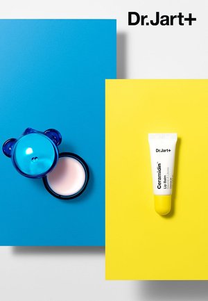 Le tube de baume à lèvres Ceramidin de Dr.Jart+ avec des accents jaunes, à côté d'un contenant en forme d'ours bleu avec une crème rose, sur des fonds bleu et jaune.