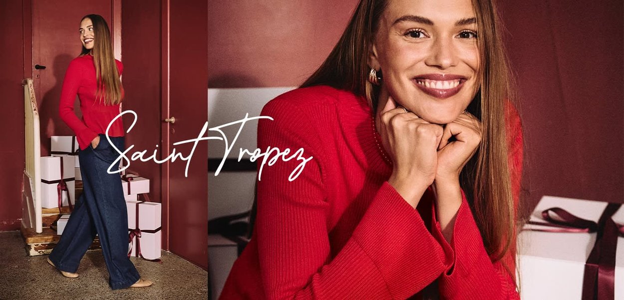 Roter, gerippter Pullover kombiniert mit dunkelblauen Jeans mit weitem Bein. Der Hintergrund zeigt weiße Geschenkboxen mit braunen Schleifen. Elegantes Innenambiente.