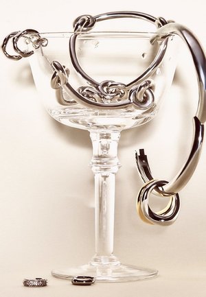 Glas-Cocktailglas mit metallischen abstrakten Schlaufen in Silber und Gold. Drei Ringe dargestellt: einer in Silber, einer in Schwarz, einer mit goldenem Akzent.