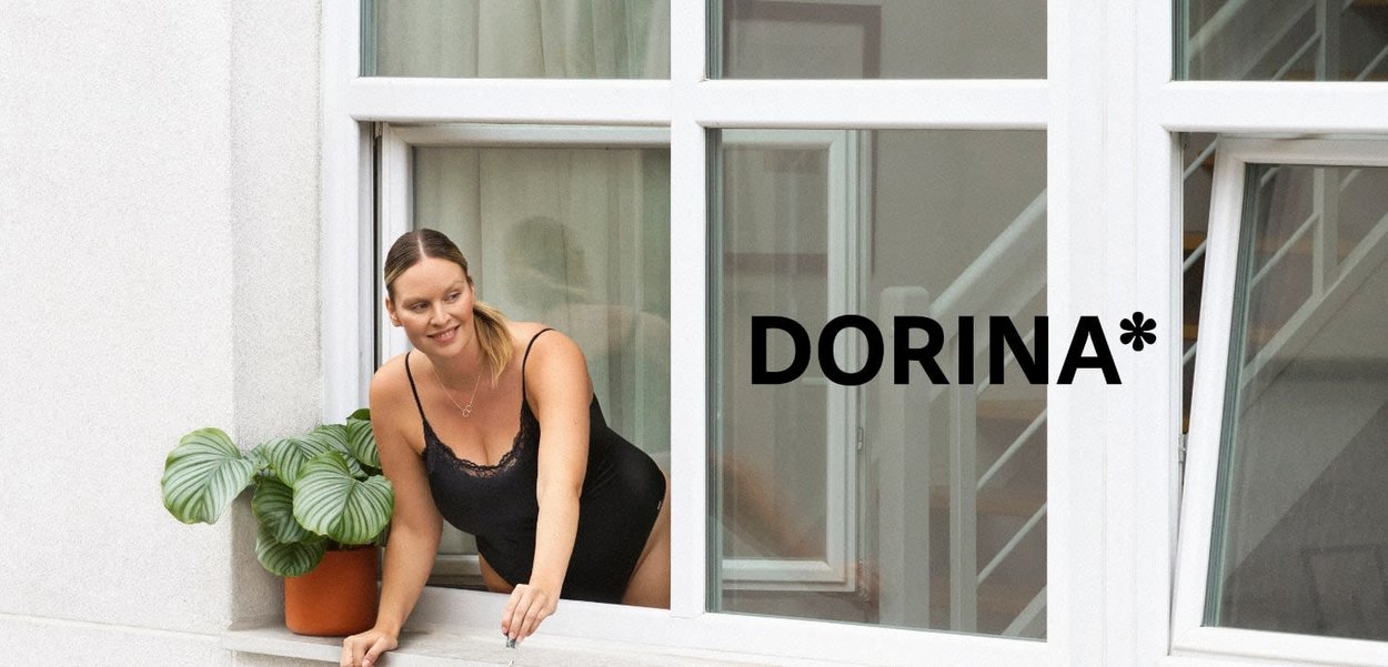 Black lingerie with lace detailing worn by a person leaning out of a window. A green potted plant sits on the ledge. White window frame.