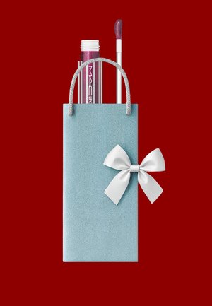Sac cadeau bleu clair texturé avec un nœud blanc, contenant un tube de gloss à lèvres transparent avec applicateur, sur fond rouge.