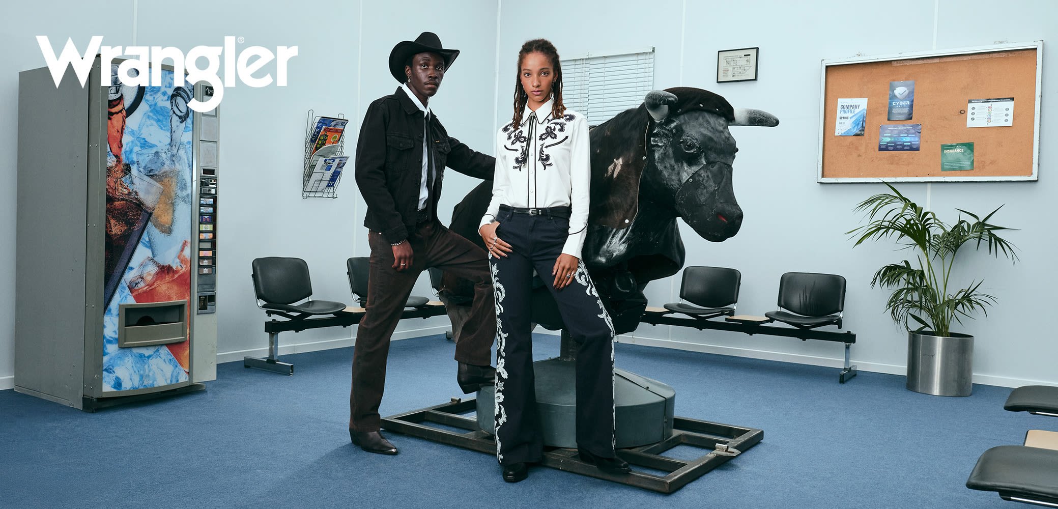 Svart denimjakke og cowboyhatt på hannlig modell, hvit brodert bluse med svarte bukser på hunnlig modell, okse-statue i uformell setting.