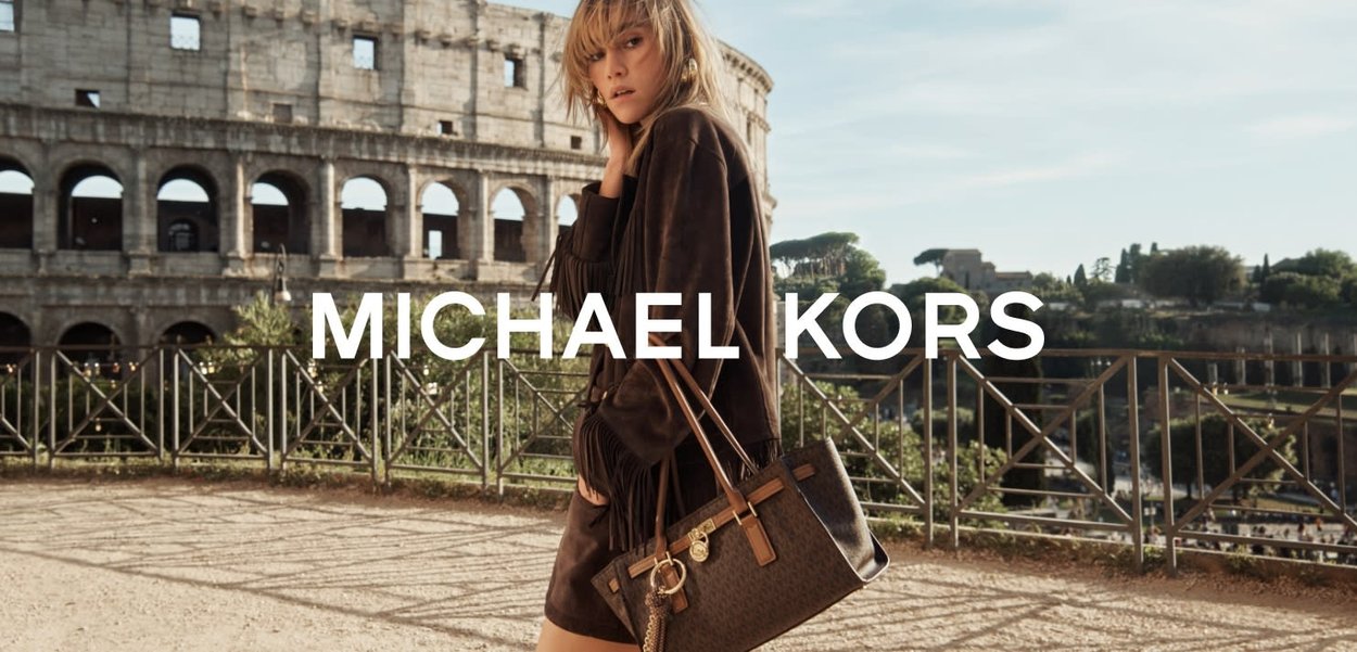 Borsa a tracolla in pelle marrone con un design testurizzato, dettagli in metallo dorato e tracolla rimovibile, ambientata in uno sfondo storico romano.