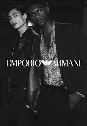 Due modelli posano fianco a fianco. Uno indossa una giacca di pelle nera; l'altro ha una camicia botton down a fantasia. I colori monocromatici dominano.