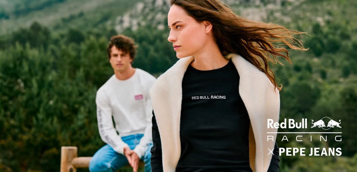 Black long-sleeve shirt with "RED BULL RACING" text, paired with a cream-colored, textured jacket. Male model in white shirt, blurred background.