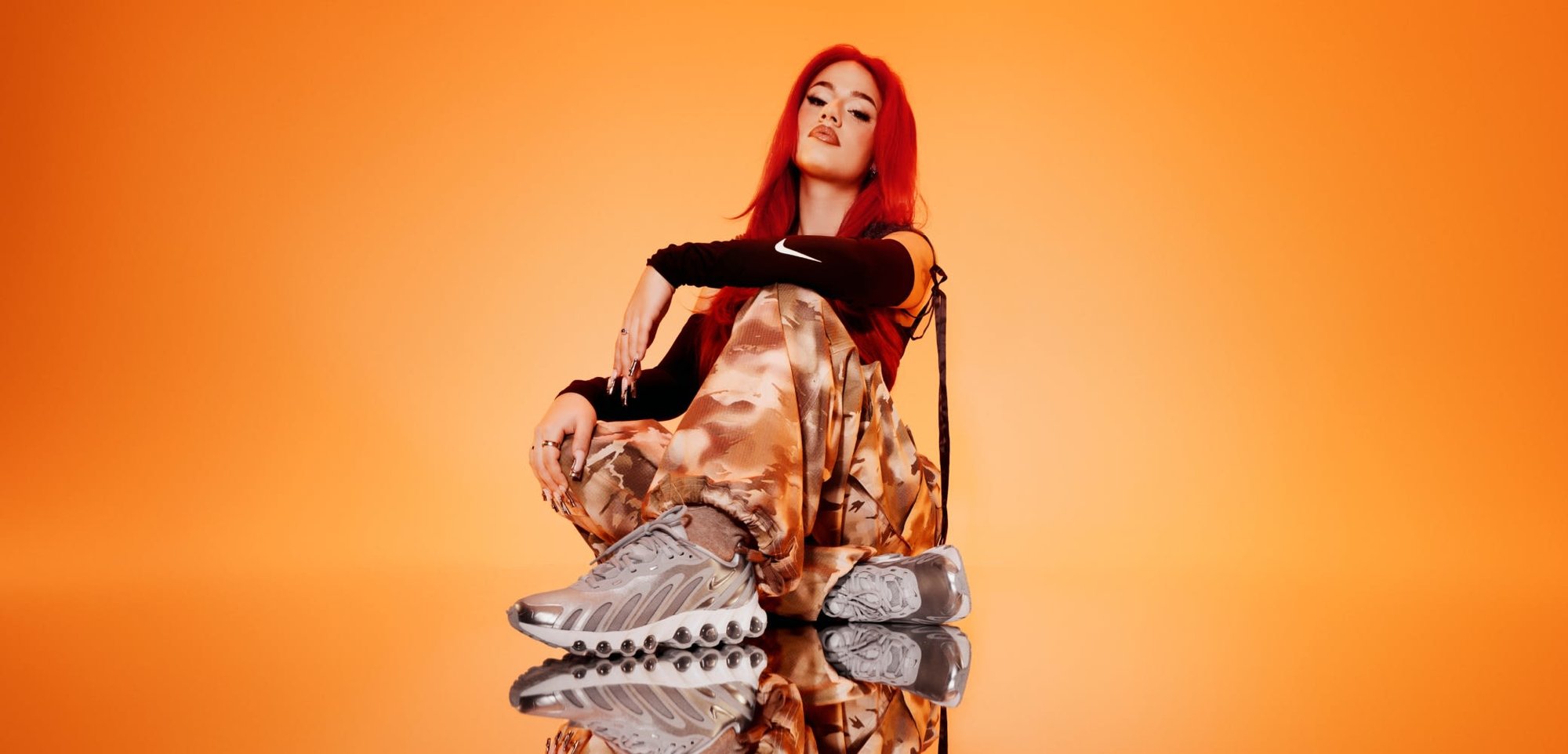 Graue Sportschuhe mit einem strukturierten Design, kombiniert mit gemusterten, hellbraunen Camouflage-Hosen. Der Hintergrund ist in einer einheitlichen orange Farbe.