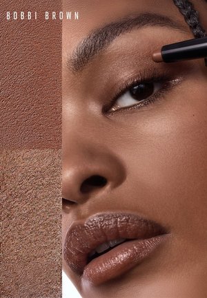 Close-up of a person applying brown eyeshadow with a stick, showcasing smooth skin and matching lip color, with Bobbi Brown branding.