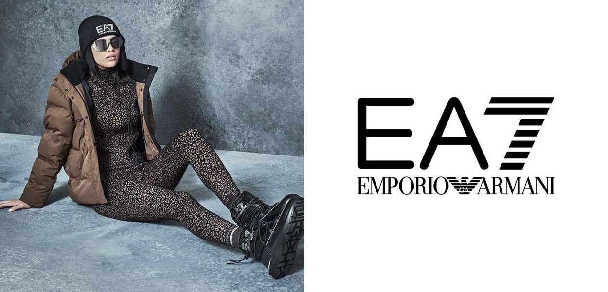 Doudoune marron portée sur une combinaison imprimée léopard noire, associée à des bottes noires à lacets et des lunettes de soleil foncées ; bonnet noir avec logo.