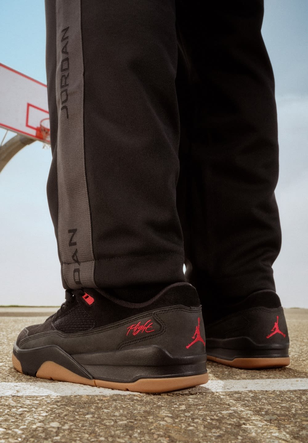 Baskets de sport noires avec des accents rouges, un dessus en suède et en maille, et des semelles en caoutchouc gomme. Le pantalon présente une bande grise avec le texte "JORDAN".