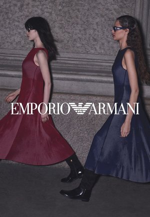 Due modellano camminano fianco a fianco, indossando abiti a maniche corte e a coste, uno rosso e l'altro blu navy. Entrambi abbinano gli abiti a stivali lucidi neri fino al ginocchio.
