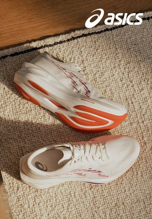 Baskets de sport blanches avec des accents orange et violet, tige en maille texturée et semelle rembourrée. Positionnées sur une surface texturée.