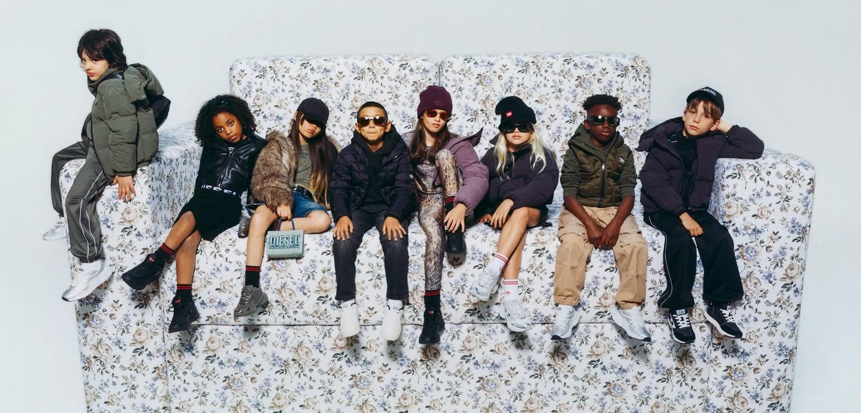 Eine Gruppe von Kindern in trendigen Outfits mit Sonnenbrillen, die auf einem blumenmusterbezogenen Sofa sitzen. Die Farben sind vielfältig und umfassen Schwarz, Grau und Olivgrün.