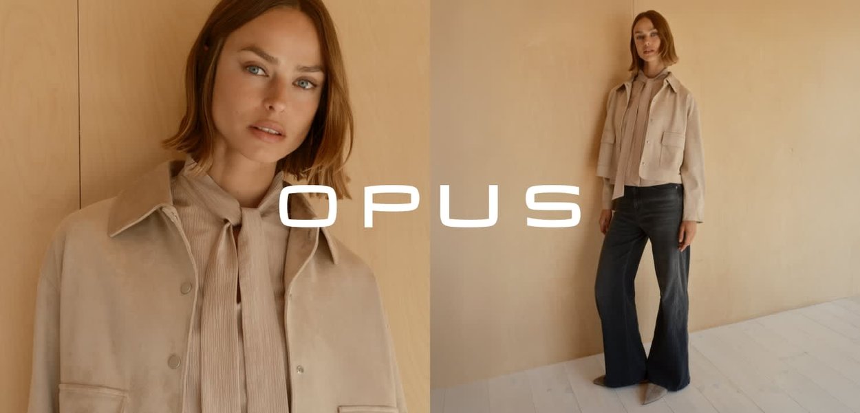 Beige suède jas met grote zakken, gecombineerd met een bleke blouse en donkere wijde spijkerbroek. Neutrale achtergrond benadrukt de outfit.