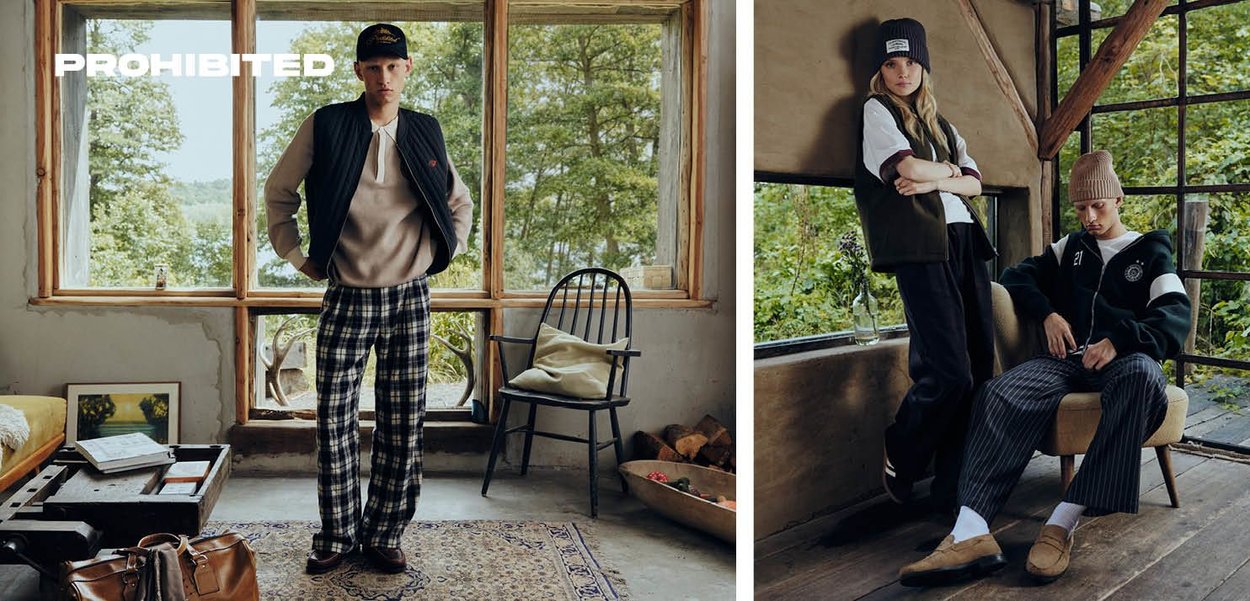 Due modelli si trovano in una stanza con grandi finestre. Uno indossa un gilet scuro, un maglione chiaro e dei pantaloni a quadri; l'altro indossa una giacca scura e pantaloni a righe.
