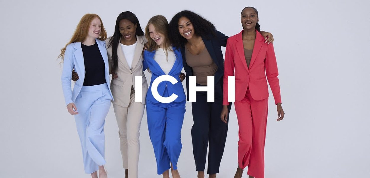 Fünf Frauen tragen maßgeschneiderte Anzüge in Pastellblau, Beige, kräftigem Blau und Rot. Die Anzüge haben Revers und passende Hosen. "ICHI" ist deutlich sichtbar dargestellt.