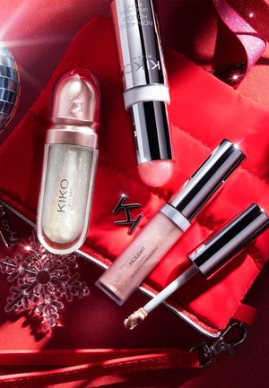 Tre prodotti di trucco KIKO Milano: un balsamo labbra scintillante in un tubetto trasparente, una matita illuminante effetto neve e un ombretto liquido rosa con applicatore, su una pochette trapuntata rossa.
