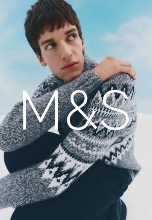 Dzianinowy szary sweter z wzorem Fair Isle w kolorze czarno-białym. Modelka siedzi, obejmując kolana, na jasnoniebieskim tle.