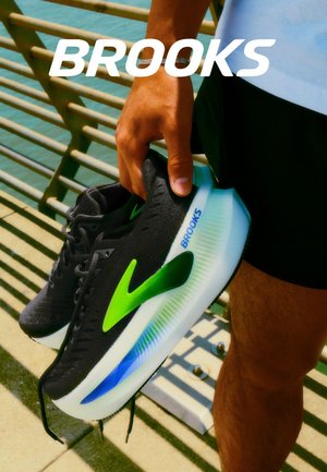 Baskets noires avec une tige texturée, des accents vert vif et une semelle d'un ton bleu arborant le logo "Brooks" sur le côté.