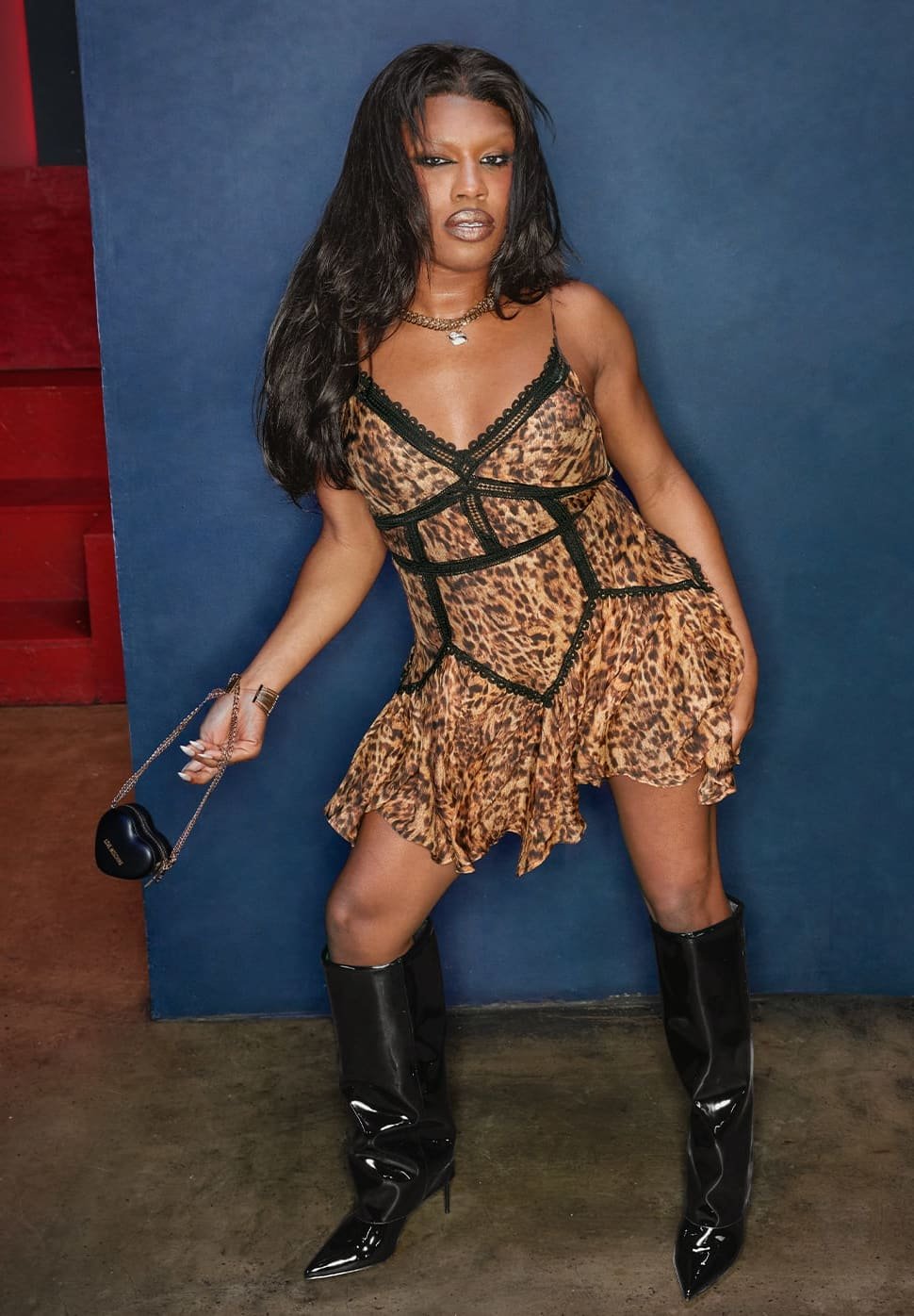 Leopardmönstrad klänning med spetskant, utsvängd kjol och smala axelband; kombinerad med knähöga, glansiga svarta stövlar och en rund svart handväska.