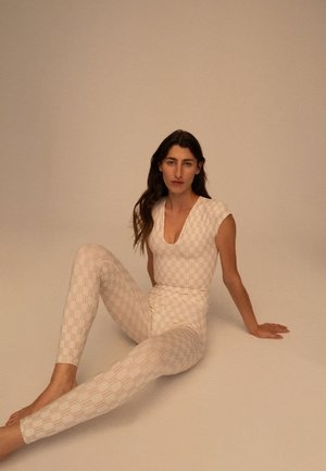 Hvit teksturert bodysuit med korte ermer og dyp V-hals, kombinert med matchende leggings med rutete mønster.