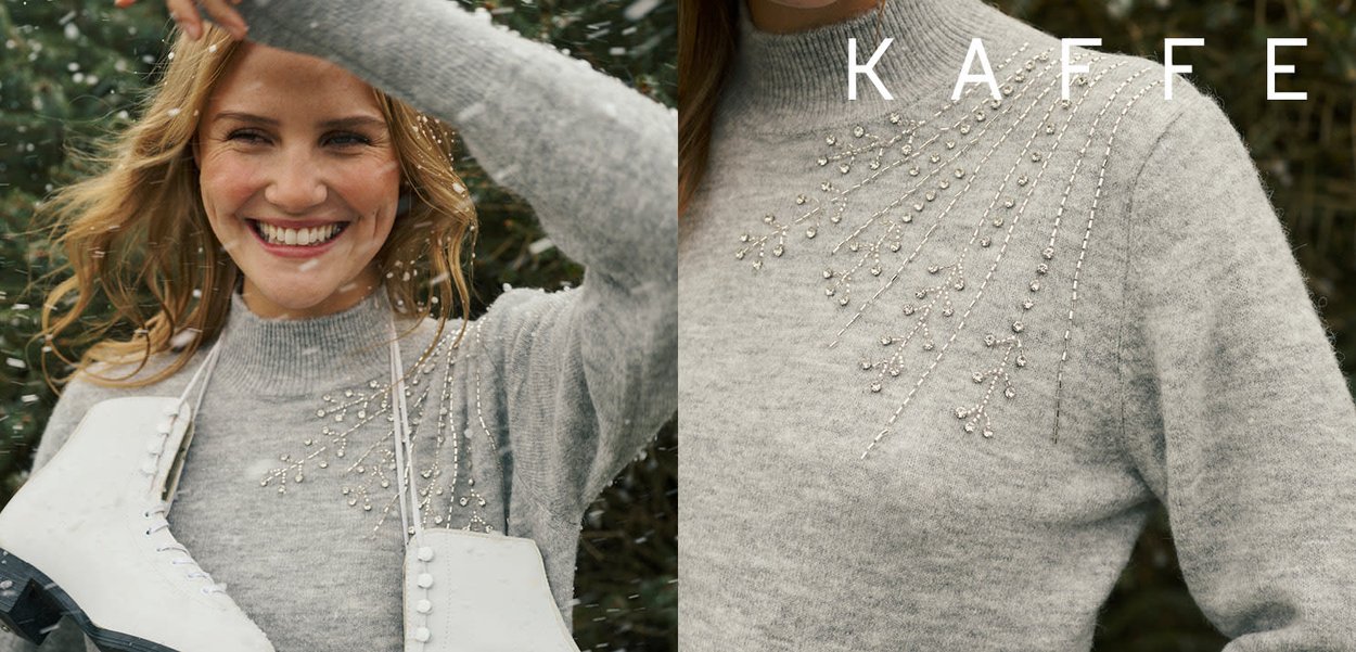 Lysegrå sweater med høj halsudskæring, der har dekorative perleakcenter, der danner blomsterlignende mønstre langs den øvre front. Blød tekstur, afslappet pasform.