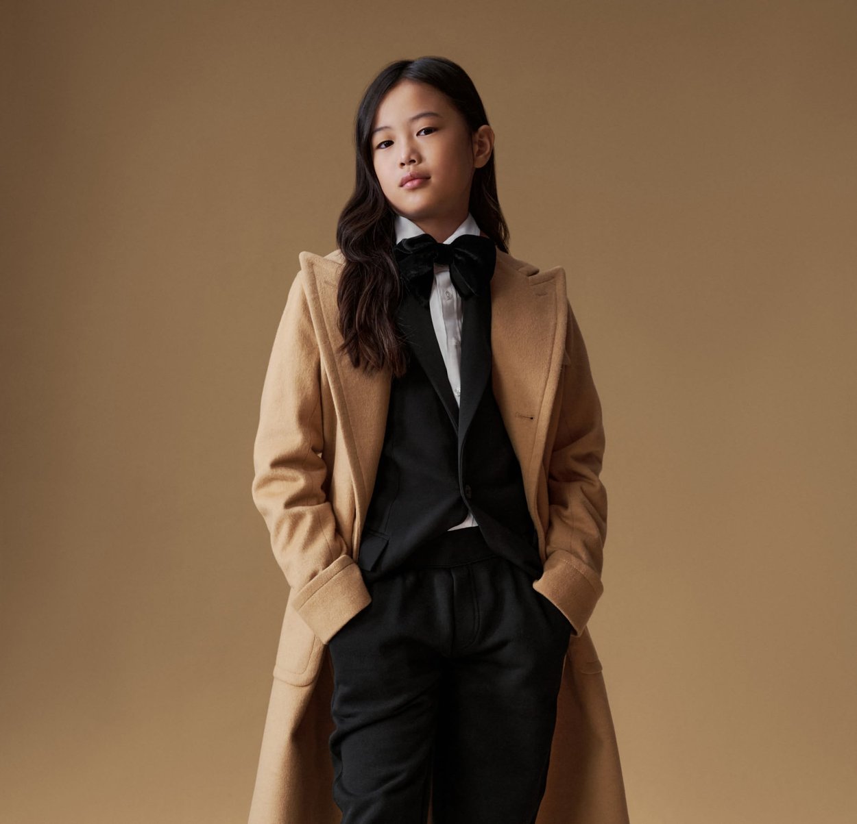 Tan ullrock över en svart kostym med vit skjorta och fluga. Har en slank design, mjuk textur och skräddarsydd passform.