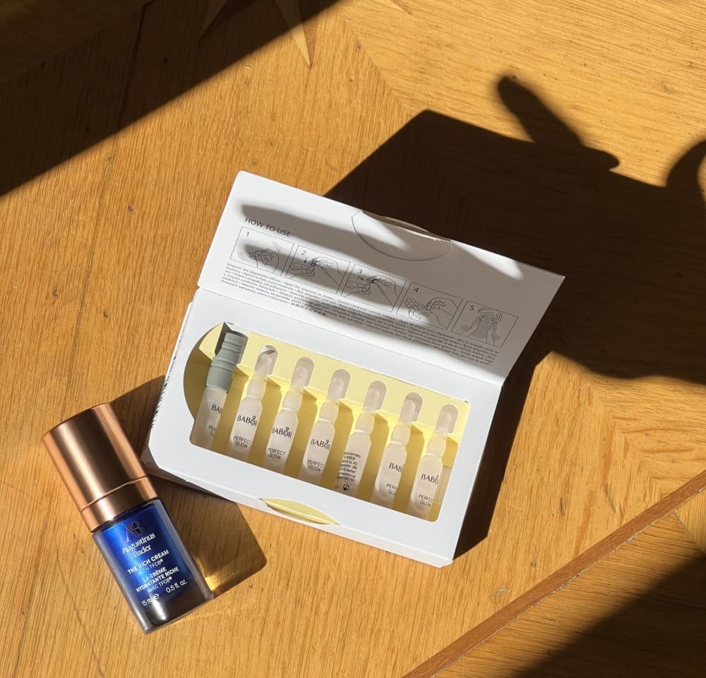 Bouteille en verre bleu avec un capuchon doré à côté d'une boîte blanche contenant des ampoules jaunes. La boîte présente des instructions d'utilisation et un étiquetage de la marque.