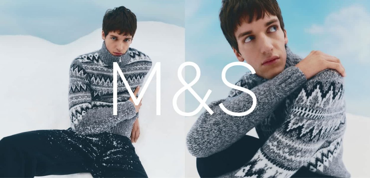 Szary dziany sweter z wysokim kołnierzem, ozdobiony geometrycznym czarno-białym wzorem. Modelka siedzi na śniegu, ubrana w czarne spodnie.