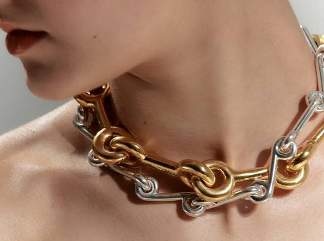 Περιδέραιο με παχιές αλυσίδες που διαθέτει αλληλοσυνδεδεμένους χρυσούς και ασημένιους μεταλλικούς κρίκους, με λεία επιφάνεια και μεγάλες κυκλικές λεπτομέρειες.