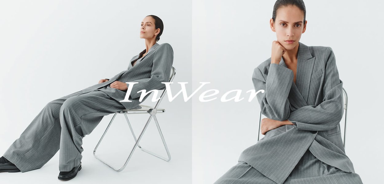 Grau gestreifter Nadelstreifen-Anzug mit lockerer Passform, weit geschnittenen Hosenbeinen und übergroßem Blazer. Model sitzt auf einem verchromten Stuhl vor einem weißen Hintergrund.