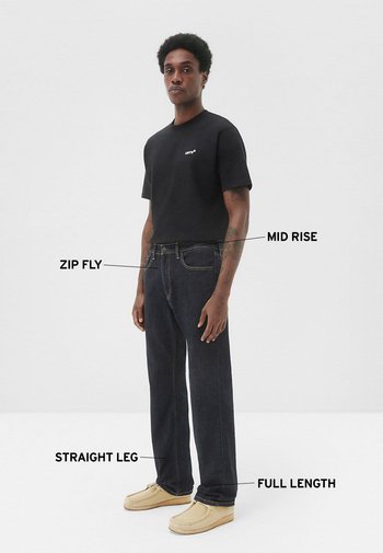 Camiseta negra de manga corta, jeans vaqueros de mezclilla oscura con cremallera a media altura, corte recto, largo completo, combinados con zapatos mocasín beige.