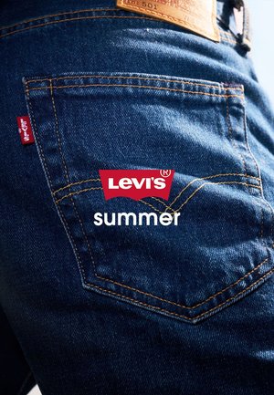 Tasca posteriore di jeans Levi's blu con cuciture visibili, etichetta rossa Levi's e patch in pelle sopra la tasca. La parola "summer" è sovrapposta.