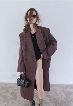 Manteau en velours côtelé bordeaux surdimensionné avec un design à double boutonnage, associé à un haut noir, un sac à main noir et des chaussettes hautes beiges.