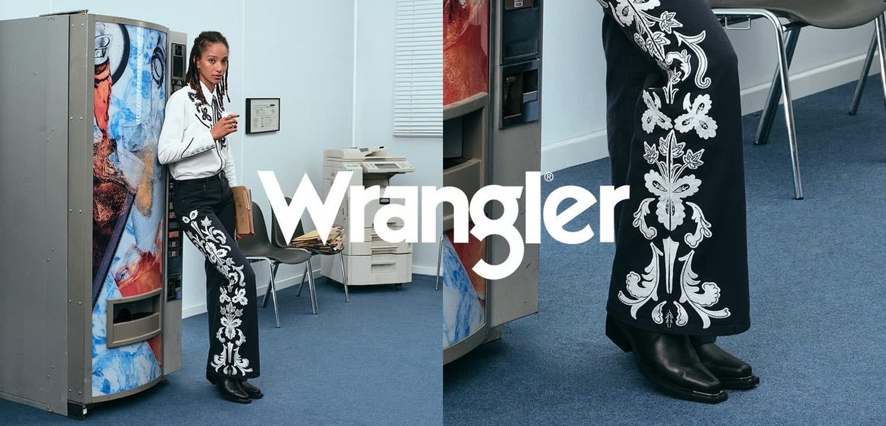 Black pants with white floral embroidery along the outer seams, paired with a white long-sleeve shirt. Setting features a vending machine.