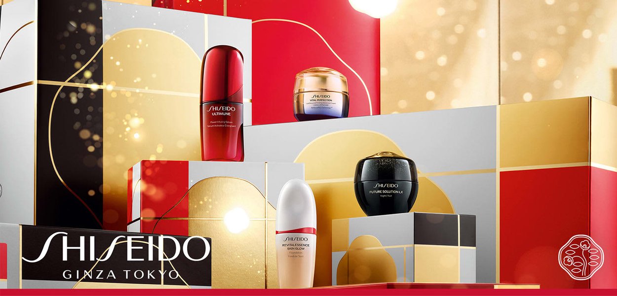 Prodotti per la cura della pelle Shiseido esposti su scatole geometriche colorate. Articoli notevoli includono una bottiglia di siero rossa e vari barattoli di crema.