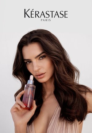 Kérastase Haaröl in einer transparenten Flasche mit einem rosa Tropfenverschluss. Die Flüssigkeit hat einen Farbverlauf von klar zu rosa. Der Hintergrund ist hellgrau.