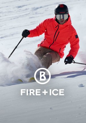 Jasnopomarańczowa kurtka narciarska z czarnymi akcentami, noszona przez narciarza na śniegu, w połączeniu z czarnym kaskiem i goglami, uchwycona w akcji na zimowym krajobrazie.