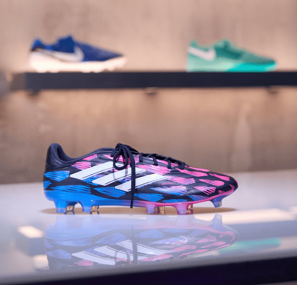 Schwarzer Fußballschuh mit blauen und pinken abstrakten Mustern, Schnürdesign, drei weiße Streifen und durchsichtiger Außensohle.