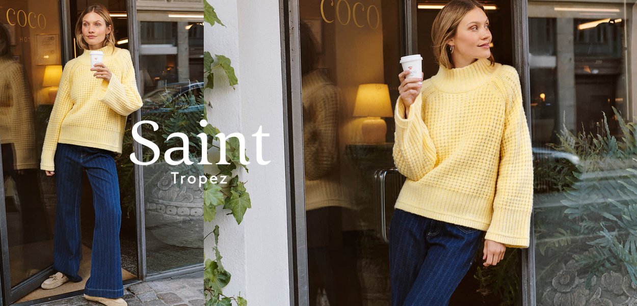 Gelber gestrickter Pullover mit hohem Kragen und lockerem Schnitt, mit einem strukturierten Muster. Kombiniert mit dunklen gestreiften Jeans und hält eine Tasse in der Hand.