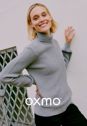 Grijze geribbelde coltrui met lange mouwen, gestructureerd breisel en iets losse pasvorm, gecombineerd met zwarte broek.